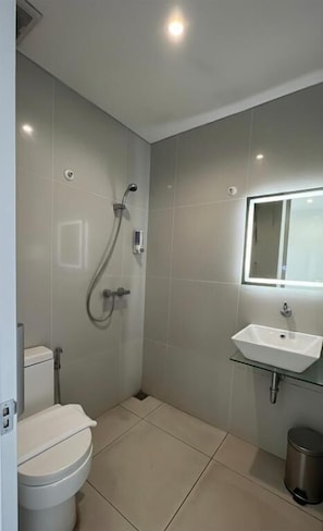 Een badkamer met toilet, douche, wastafel en spiegel.