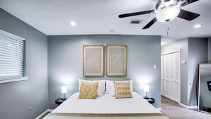 Une chambre à coucher comprenant un lit, deux tables de chevet avec des lampes, un ventilateur de plafond et une porte donnant sur un placard.