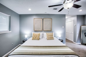 A bedroom with a bed, two bedside tables with lamps, a ceiling fan, and a door leading to a closet.