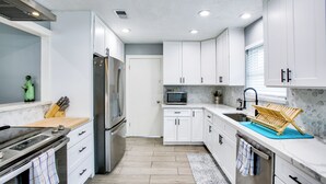 Une cuisine moderne avec des meubles blancs, des appareils en acier inoxydable et un porte-serviettes bleu.
