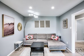 Ein Wohnzimmer mit grauem Sofa, einem schwarzen Couchtisch und einem großen gerahmten Bild an der Wand.