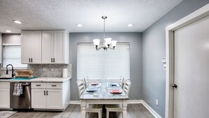Une cuisine avec des meubles blancs, une table à manger dressée pour quatre personnes et un lustre.