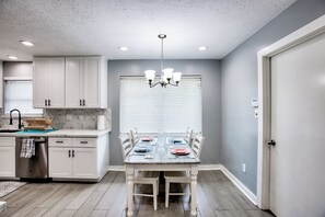 A kitchen with white cabinets, a dining table set for four, and a chandelier. - FIFA Basecamp - NASA - Med Center - Galveston - NRG - Kemah Hub! (Houston)