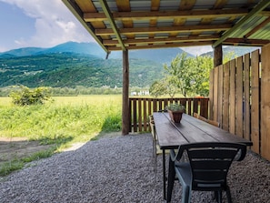 Ein überdachter Außenbereich mit Tisch und Stühlen, einem Blumentopf und Blick auf eine grüne Landschaft mit Bergen im Hintergrund.