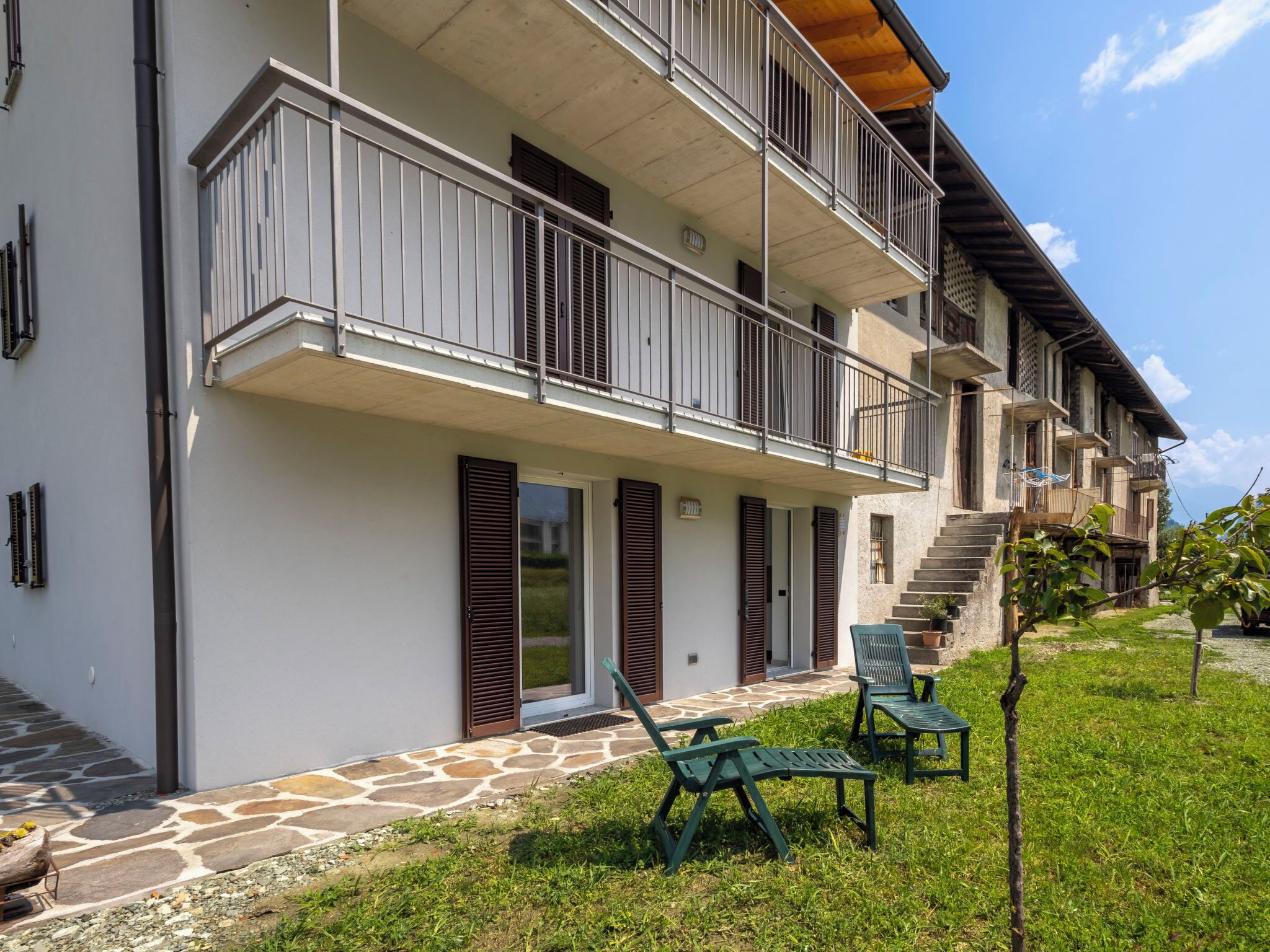 Un immeuble à plusieurs étages doté de balcons, d’une entrée pavée de pierres et d’un espace extérieur aménagé pour s’asseoir.