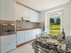 A modern kitchen with white cabinets, a built-in oven, and a dining area with a table set for two. - Isola Verde Garden Home by Interhome (Valtellina)
