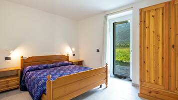 A bedroom with a wooden bed, bedside tables, a wardrobe, and a view of a green landscape through a glass door.