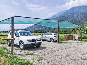 Two cars parked under a shaded area with a mountainous backdrop. - Isola Verde Garden Home by Interhome (Valtellina)