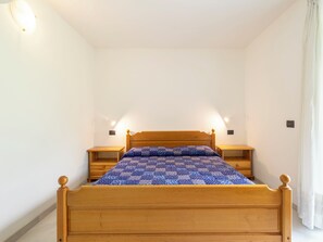 A single bed with a wooden frame and a blue patterned bedspread in a room with white walls and two bedside tables. - Isola Verde Garden Home by Interhome (Valtellina)