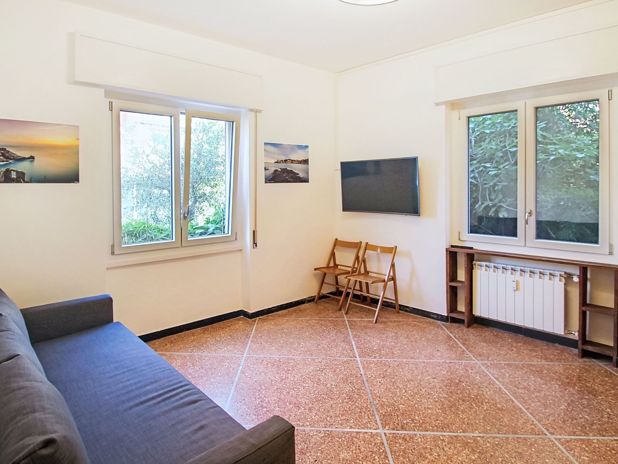 Un salon avec un canapé, deux fauteuils, un téléviseur et un radiateur.