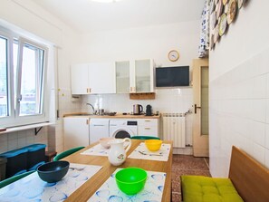 A compact kitchen with a washing machine, a dining table with bowls, and a TV mounted on the wall. - Ardesia by Interhome (Lavagna)