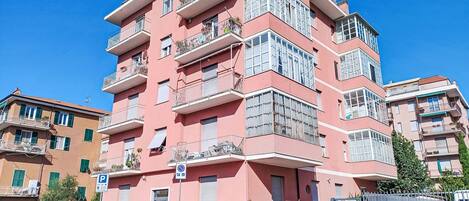 A multi-story building with balconies, a parking sign, and construction barriers.