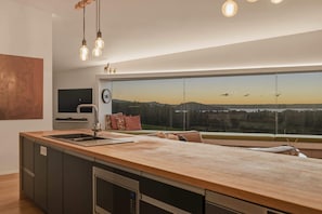 Eine moderne Küche mit einer großen Kochinsel, einem Einbauofen und Blick auf eine untergehende Landschaft.