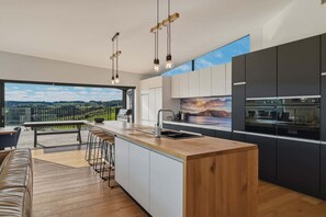 Eine moderne Küche mit einer großen Kochinsel, Barhocker, Blick ins Freie und einem großen Fenster.