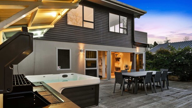 A modern house with a hot tub, patio furniture, and a well-lit interior.