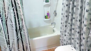 A bathroom with a bathtub, shower, toilet, and a small shelf with toiletries. - Quiet, Humble, 1-bedroom cabin in charming North Pole perfect for a cozy getaway (North Pole)