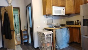A compact kitchen with wooden cabinets, a microwave, a toaster, and a refrigerator. - Quiet, Humble, 1-bedroom cabin in charming North Pole perfect for a cozy getaway (North Pole)