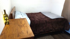 A small room with a wooden table, a bottle of wine, a brown bed with a blanket, and a patterned rug. - Quiet, Humble, 1-bedroom cabin in charming North Pole perfect for a cozy getaway (North Pole)