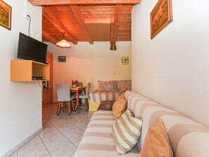 Ein kompakter Wohnbereich mit einer Couch, einem Esstisch mit Stühlen, einem an der Wand befestigten Fernseher und einer Decke mit freiliegenden Holzbalken.