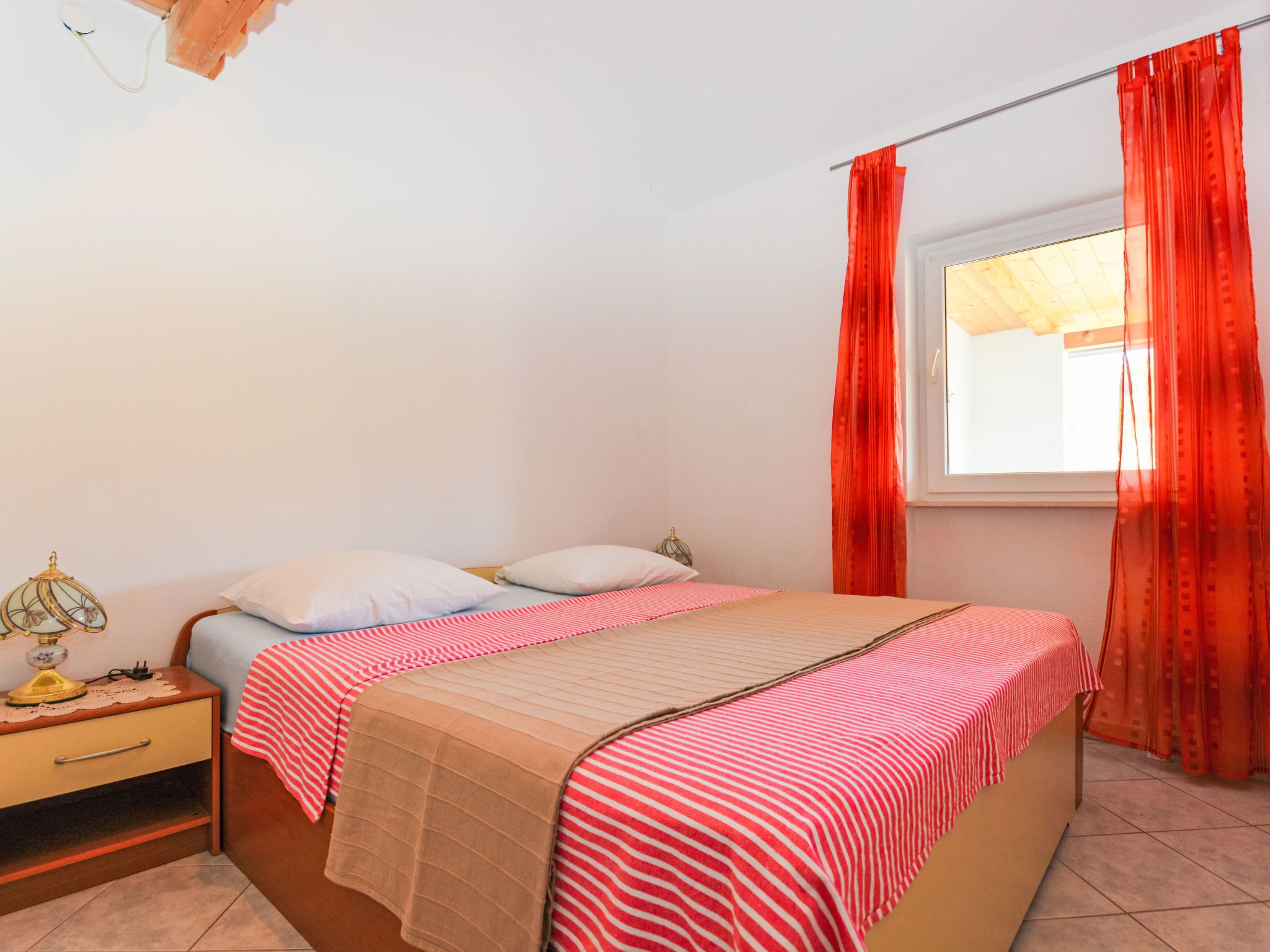 Une chambre à coucher avec un lit, une table de chevet, une lampe et une fenêtre avec des rideaux.