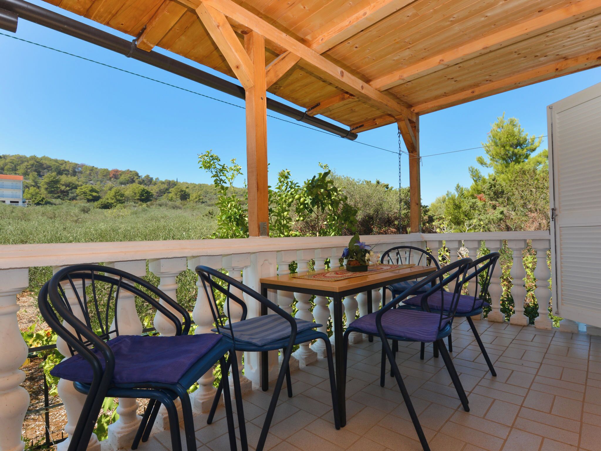 Un patio cubierto al aire libre con una mesa y sillas, y vistas a la vegetación y colinas al fondo.