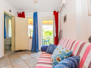 Ett rum med en randig soffa, ett litet fönster med gardiner, en dörr som leder ut till en balkong och en krukväxt på fönsterbrädan.
