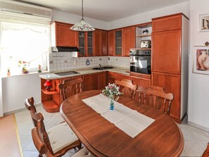 A kitchen with wooden cabinets, a stove, and a dining table with chairs. - Apartment Jako by Interhome (Trogir/Slatine)