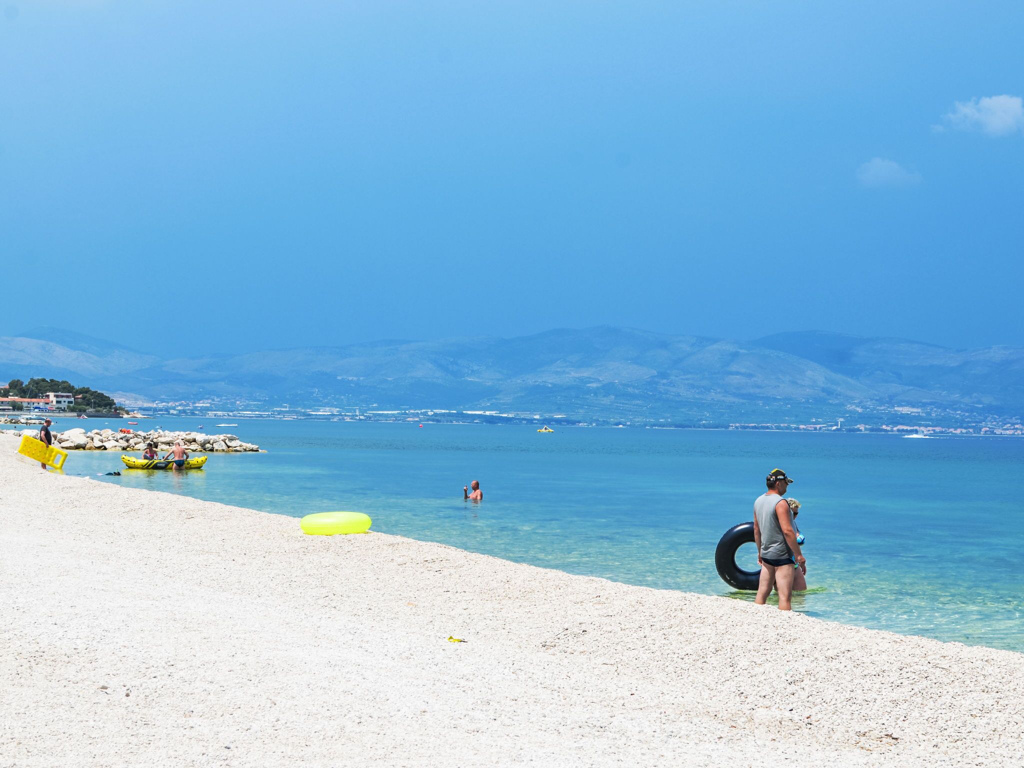 A beach with clear water, a rocky shoreline, and distant mountains.