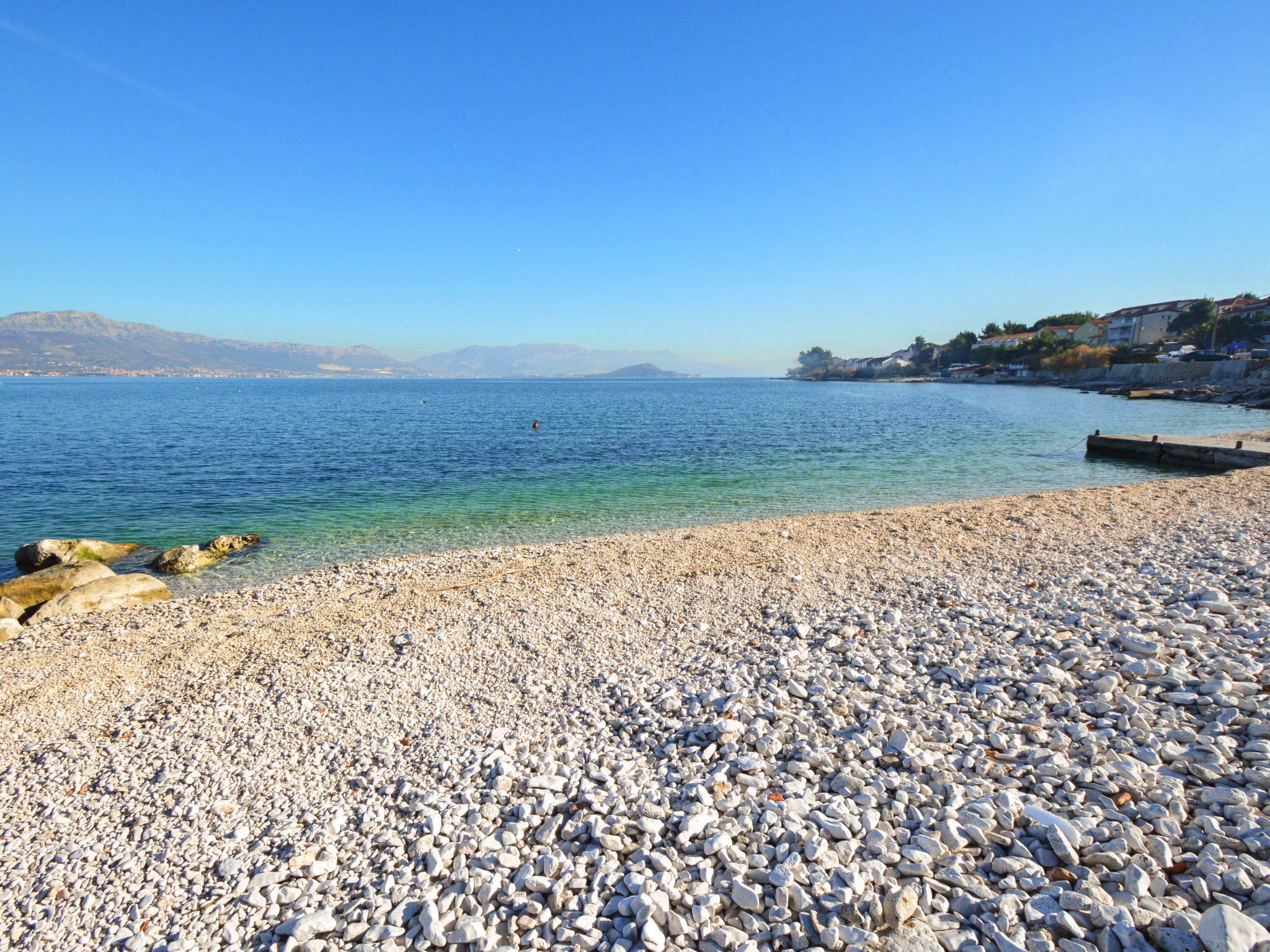 Une plage de galets avec une eau cristalline et des montagnes qui se dessinent à l'horizon.
