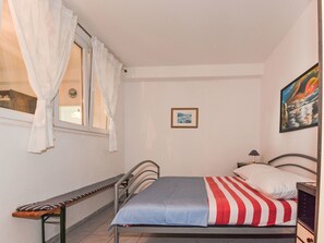 Ein Schlafzimmer mit Bett, einer Bank, einem Fenster mit Vorhängen, einem gerahmten Bild an der Wand und einem Gemälde über dem Bett.