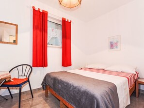 A bedroom with a bed, a chair, a window with red curtains, a bedside table, and a wall-mounted lamp. - Apartment Jako by Interhome (Trogir/Slatine)