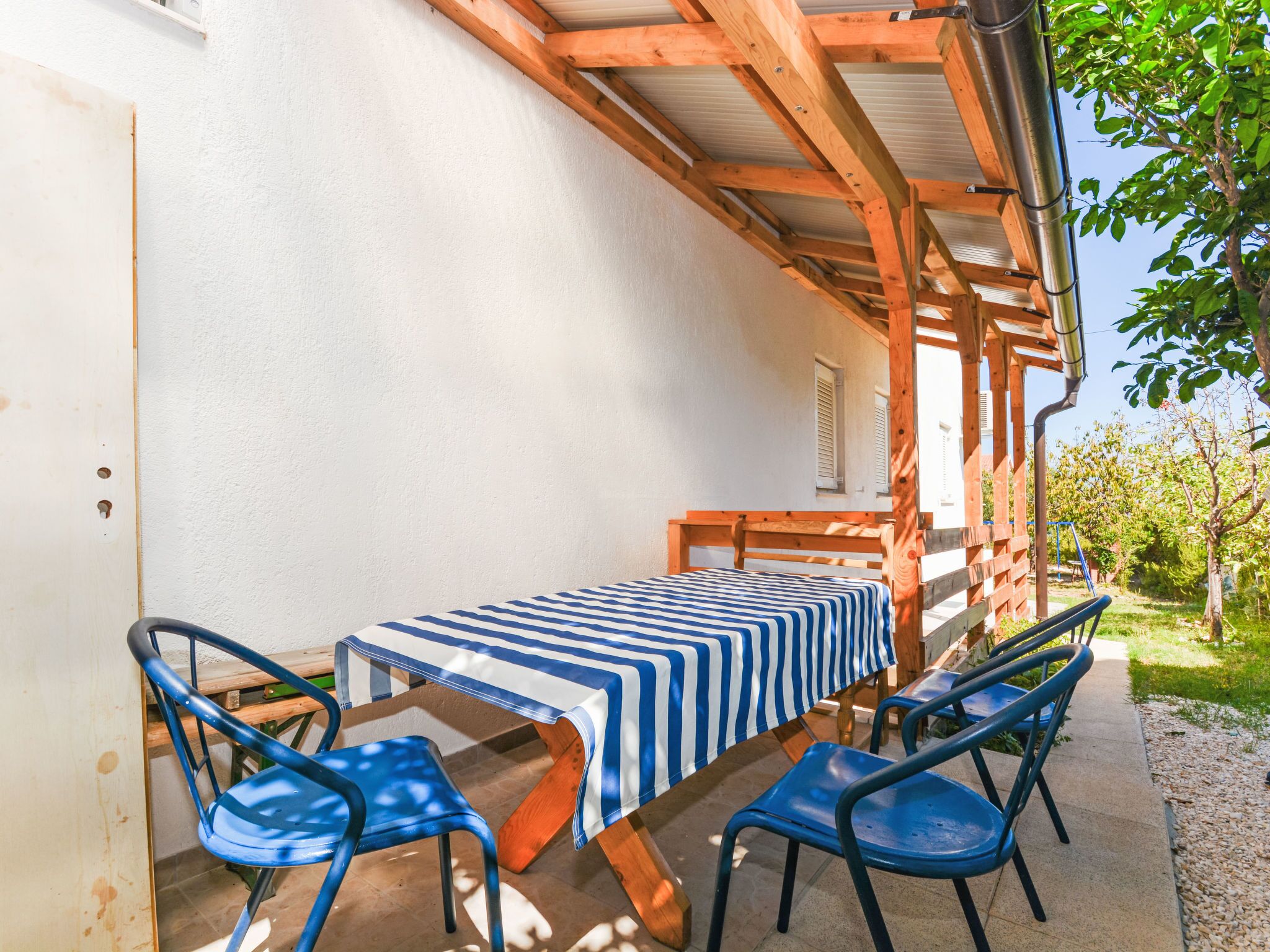 Um alpendre coberto com mesa e cadeiras, um banco de madeira e vista para um jardim.