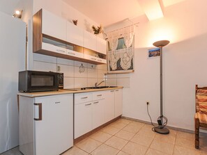 Eine kompakte Küche mit weißen Schränken, einer Mikrowelle, einem Spülbecken und einer Stehlampe.