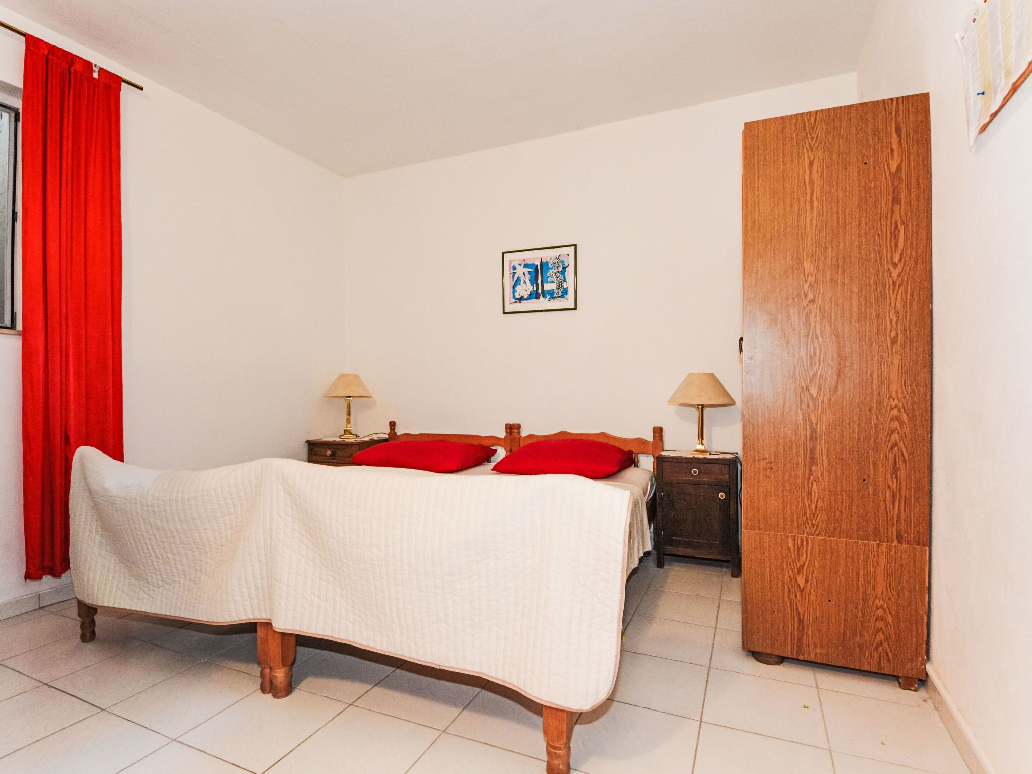 Une chambre à coucher comprenant un lit, deux tables de chevet, une armoire en bois et un tableau accroché au mur.