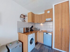 A compact kitchen with wooden cabinets, a washing machine, a dishwasher, and a small countertop with a coffee machine. - Palm Beach by Interhome (Le Barcarès)