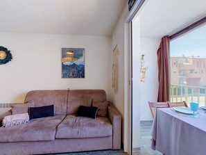 Ein Wohnzimmer mit einer Couch, einem Gemälde und Blick auf Gebäude durch ein Fenster.