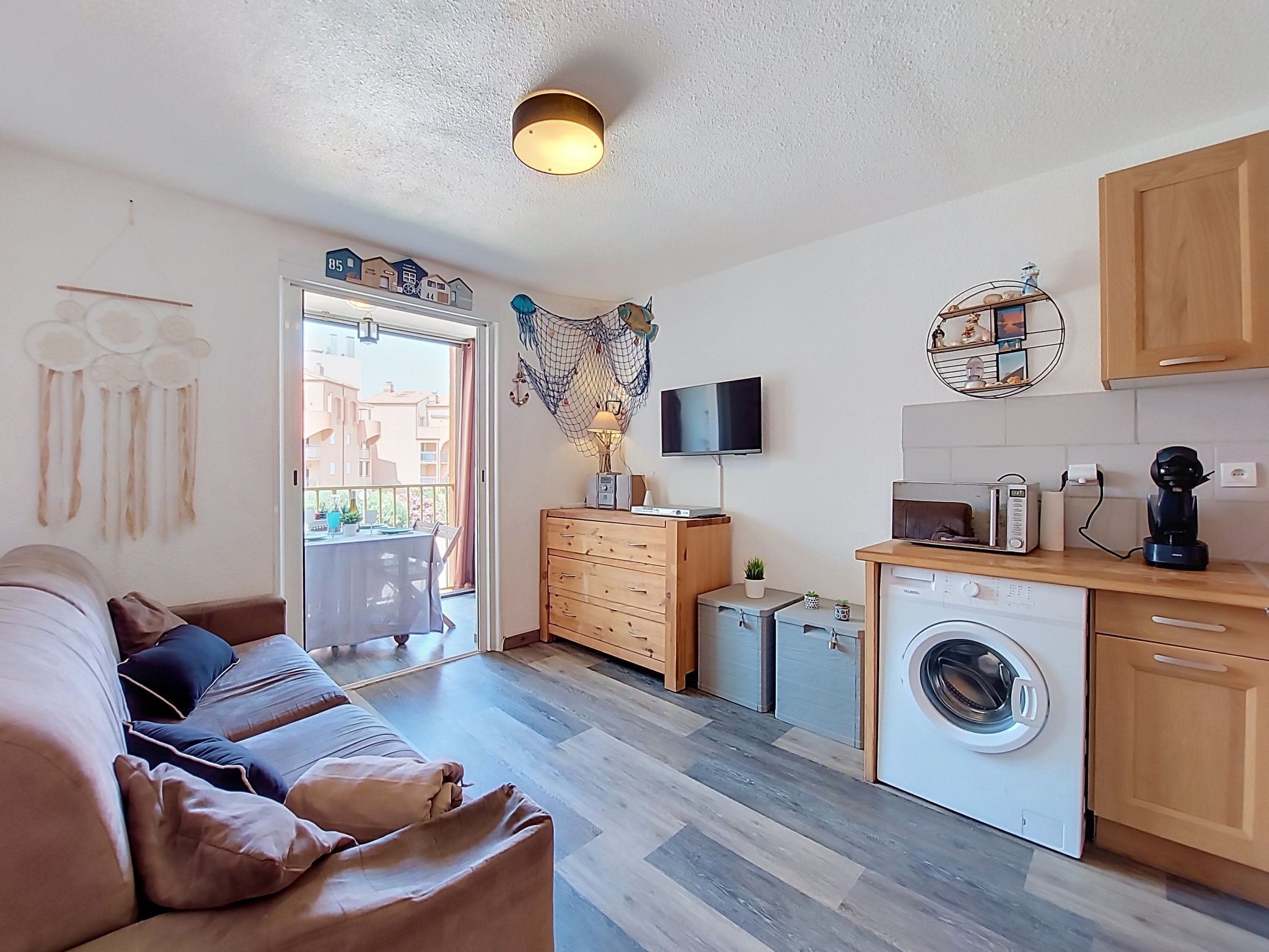 Un espacio habitable pequeño con sofá, kitchenette, lavadora y televisor.