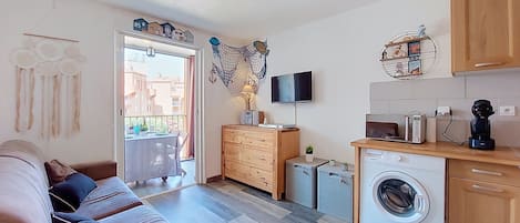 A compact living space with a sofa, kitchenette, washing machine, and a TV.