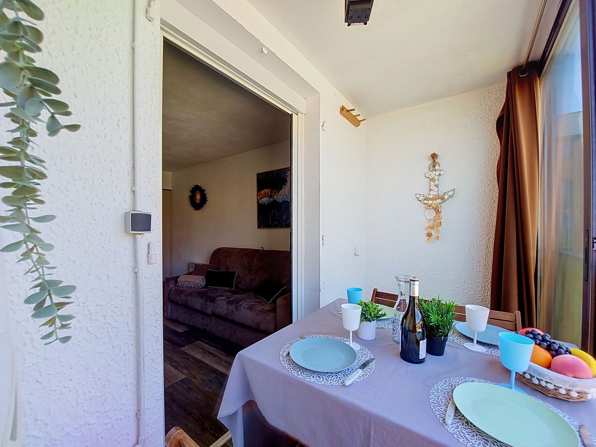 A dining area with a table set for two, a bottle of wine, and a fruit basket.