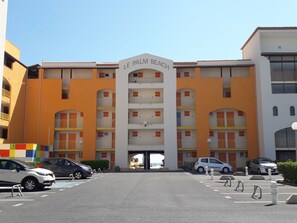 Ein mehrstöckiges Hotel mit Balkonen, einem Parkplatz und blauem Himmel.
