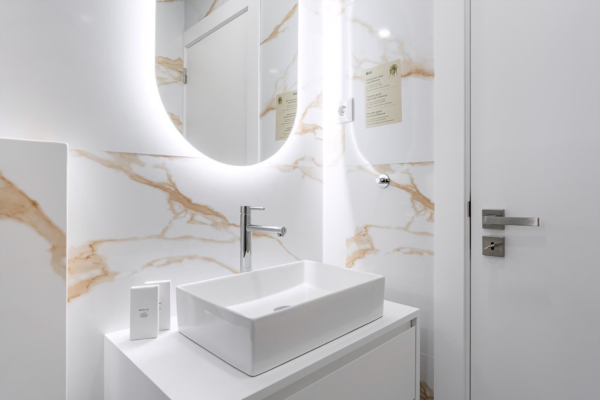 Un baño moderno con lavamanos de mármol blanco, un espejo y una puerta con manija.
