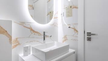 Un baño moderno con lavamanos de mármol blanco, un espejo y una puerta con manija.