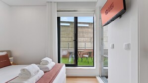 Habitación de hotel con cama, televisor, ventana con vista a un balcón y una puerta corrediza.