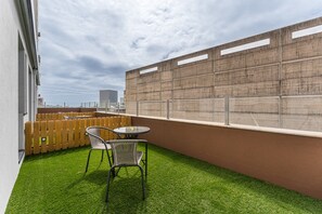 Una terraza en la azotea con césped artificial, una valla de madera y una mesa y sillas de metal.