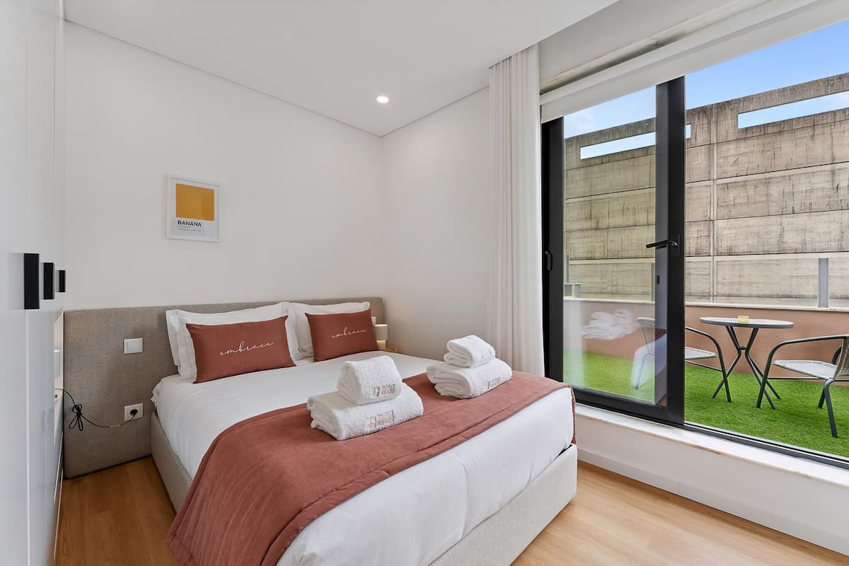 Habitación de hotel con cama, ventana, balcón con sillas e imagen colgada en la pared.