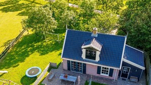 A two-story house with a blue roof, a patio with outdoor furniture, and a fenced backyard. - Fantastic family home with large garden (Hippolytushoef)