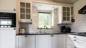 A kitchen with white cabinets, a black countertop, a window, and a built-in oven. - Fantastic family home with large garden (Hippolytushoef)