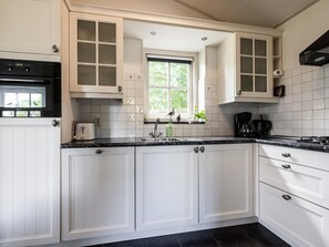 A kitchen with white cabinets, a black countertop, a window, and a built-in oven. - Fantastic family home with large garden (Hippolytushoef)