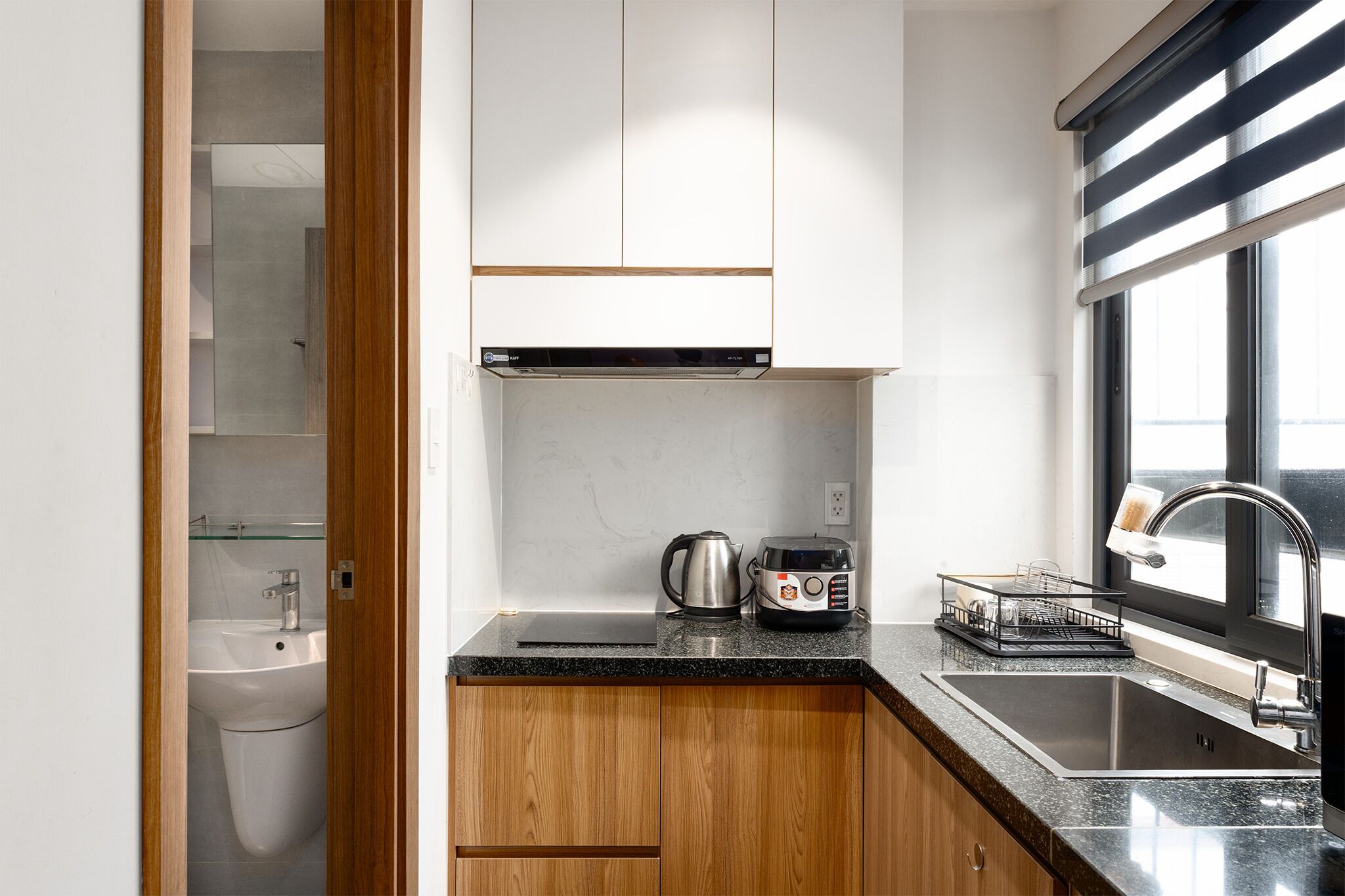 A compact kitchen with a sink, a kettle, a toaster, and a dish rack.