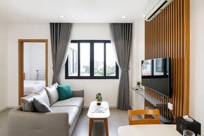 A modern living room with a sofa, a coffee table, a TV, and a view of the outside. - Ninety Six Thao Dien by DNM Hospitality (Ho Chi Minh City)